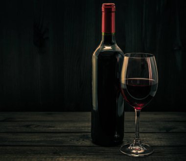 Bir şişe kırmızı şarap ve eski ahşap bir masada bir bardak kırmızı şarap.