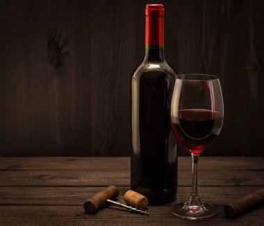 Bottle of red wine with a glass, corkscrew and cuban cigar on an old wooden table 