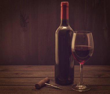 Bir şişe kırmızı şarap ve eski ahşap bir masada tirbuşon.