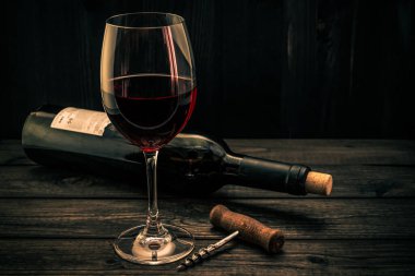Bir şişe kırmızı şarap ve eski ahşap bir masada tirbuşon.