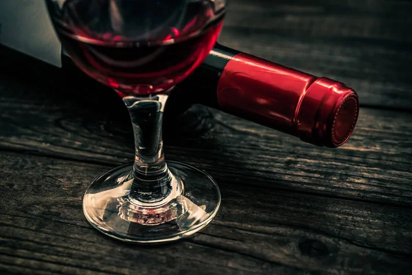 古い木製のテーブルの上に赤ワインのガラスと赤ワインのボトル — ストック写真