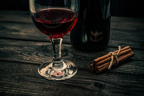 古い木製のテーブルの上に赤ワインとシナモンスティックのガラスと赤ワインのボトル — ストック写真