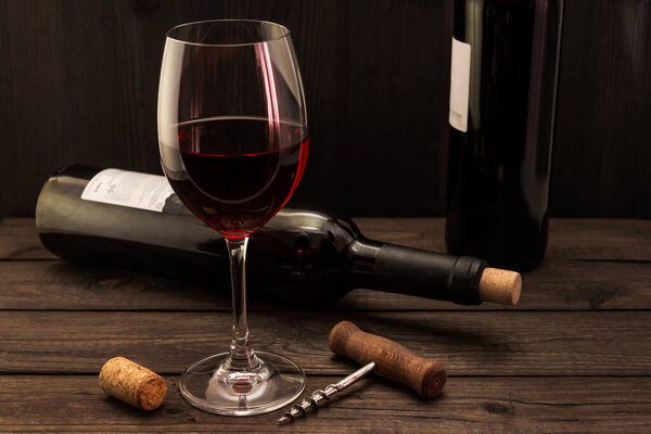 Two bottles of red wine with a glass and corkscrew with cork