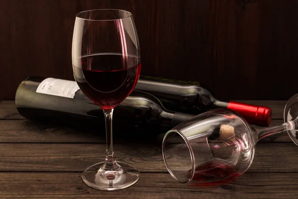 Two bottles of red wine with two glasses on an old wooden table.