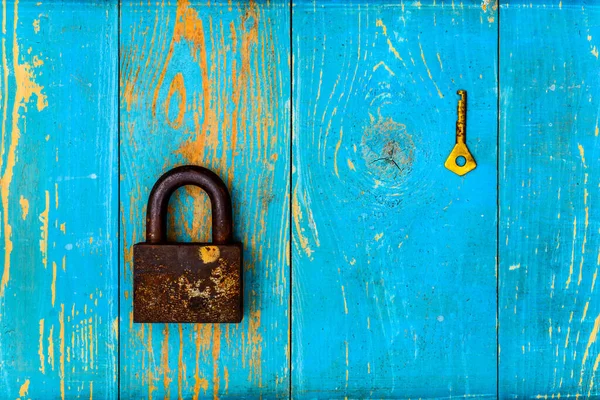 Ancient and rusty closed padlock with key on old wooden table