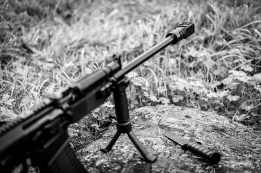 Bir çift ayaklı tüfek ve çimenlikteki bir kayanın üzerinde savaş bıçağı.