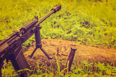 Tüfek kayanın üzerinde boş kabukları olan bir bipod üzerinde duruyor. 