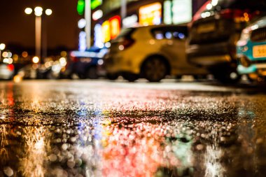 Park yerindeki alışveriş merkezinde yağmurlu bir gece, sıra sıra park edilmiş arabalar..