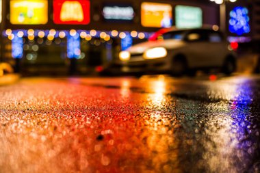 Park yerindeki alışveriş merkezinde yağmurlu bir gece, sıra sıra park edilmiş arabalar..