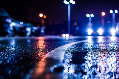 Park yerindeki alışveriş merkezinde yağmurlu bir gece, sıra sıra park edilmiş arabalar..