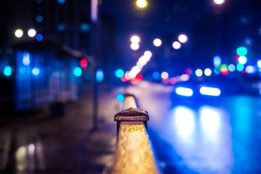 Büyük şehirde karanlık bir gece, otobüs durağı ve farlar.