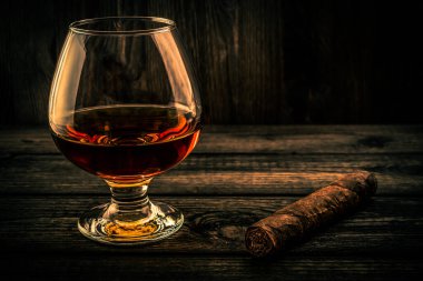 Glass of brandy and cuban cigar on a wooden table. 