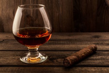 Glass of brandy and cuban cigar on a wooden table. 