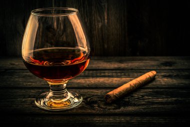 Glass of brandy and cuban cigar on a old wooden table. 