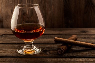 Glass of brandy and two different cuban cigars on a old wooden table 