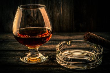 Glass of brandy and glass ashtray and cuban cigar on a old wooden table 