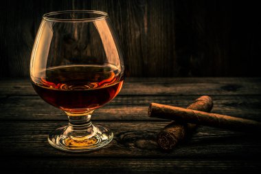 Glass of brandy and two different cuban cigars on a old wooden table 