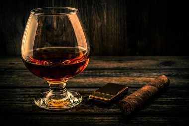 Glass of brandy and cuban cigar with golden lighter on an old wooden table