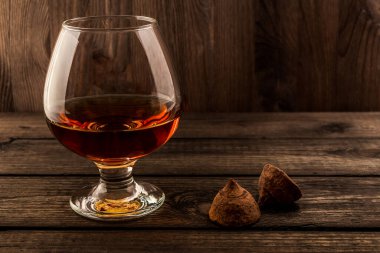 Glass of brandy and a couple of chocolate truffles on an old wooden table