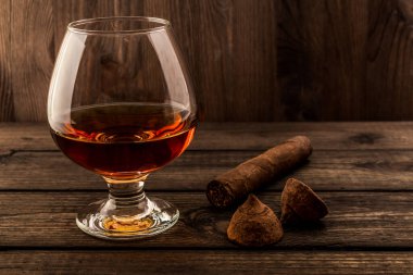 Glass of brandy and a couple of chocolate truffles with cuban cigar on an old wooden table 