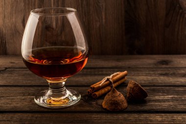 Glass of brandy and a couple of chocolate truffles with cinnamon on an old wooden table 