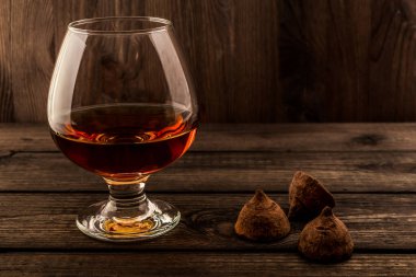 Eski ahşap bir masada bir bardak brendi ve çikolatalı trüf.. 