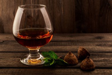 Eski ahşap bir masada bir bardak brendi ve çikolatalı trüf.. 