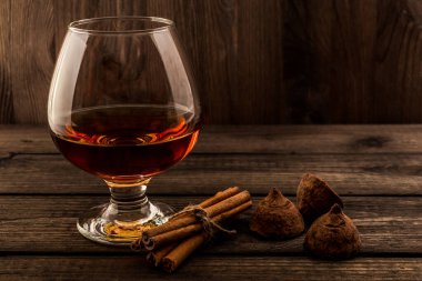 Glass of brandy and a couple of chocolate truffles with cinnamon on an old wooden table 