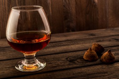 Eski ahşap bir masada bir bardak brendi ve çikolatalı trüf.. 