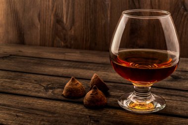 Eski ahşap bir masada bir bardak brendi ve çikolatalı trüf.. 