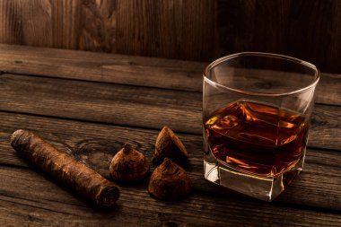 Glass of brandy and a couple of chocolate truffles with cuban cigar on an old wooden table 