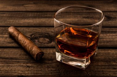Glass of brandy and cuban cigar on an old wooden table. Close up