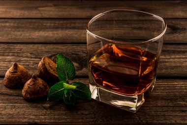 Eski ahşap bir masada bir bardak brendi ve çikolatalı trüf.. 