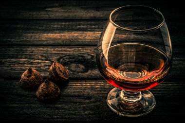 Eski ahşap bir masada bir bardak brendi ve çikolatalı trüf.. 