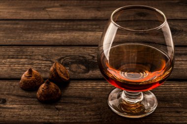 Eski ahşap bir masada bir bardak brendi ve çikolatalı trüf.. 