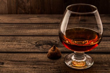 Glass of brandy and a chocolate truffle on an old wooden table. 