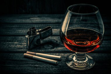 Glass of brandy with two cigarettes and lighter on a old wooden table 