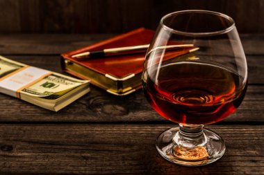 Bir bardak brendi ve altın kalemli deri defter.