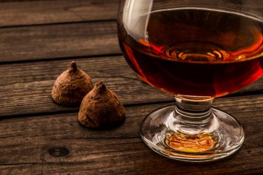 Glass of brandy and a couple of chocolate truffles on an old wooden table