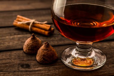 Glass of brandy and a couple of chocolate truffles with cinnamon on an old wooden table 