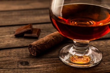 Glass of brandy and a chocolate with cuban cigar on an old wooden table
