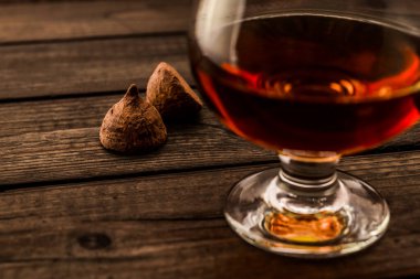 Glass of brandy and a couple of chocolate truffles on an old wooden table