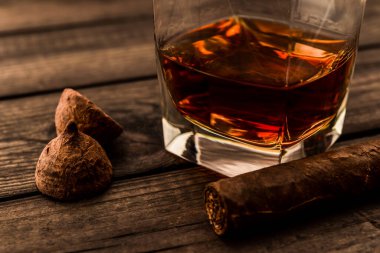 Glass of brandy and a couple of chocolate truffles with cuban cigar on an old wooden table 