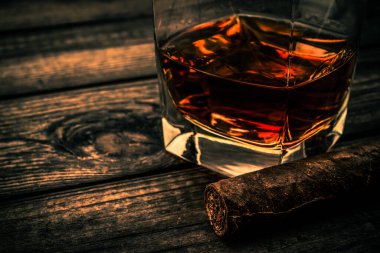 Glass of brandy and cuban cigar on an old wooden table. Close up