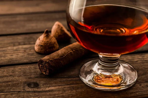 Glass of brandy and a couple of chocolate truffles with cuban cigar on an old wooden table 