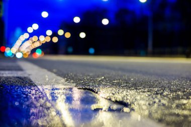 Gece şehir ışıkları gece yolundaki su birikintisine yansıyor..