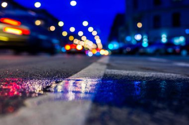 Gece şehir ışıkları gece yolundaki su birikintisine yansıyor..