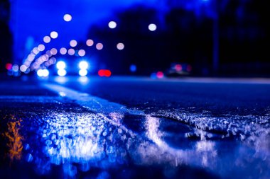 Gece şehir ışıkları gece yolundaki su birikintisine yansıyor..