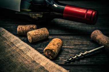 Bottle of red wine and piece of canvas with corkscrew and corks on an old wooden table 