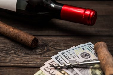 Bottle of red wine and cuban cigar with money and corkscrew on an old wooden table 